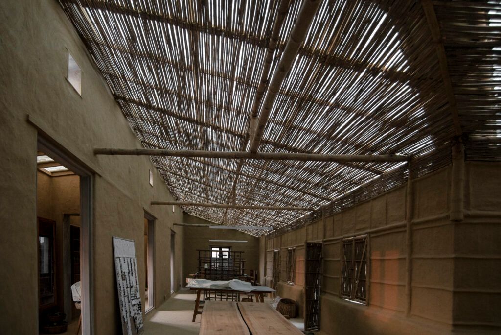 A hallway in the Ganga Maki Textile Studio complex with rammed earth walls and thatch roof