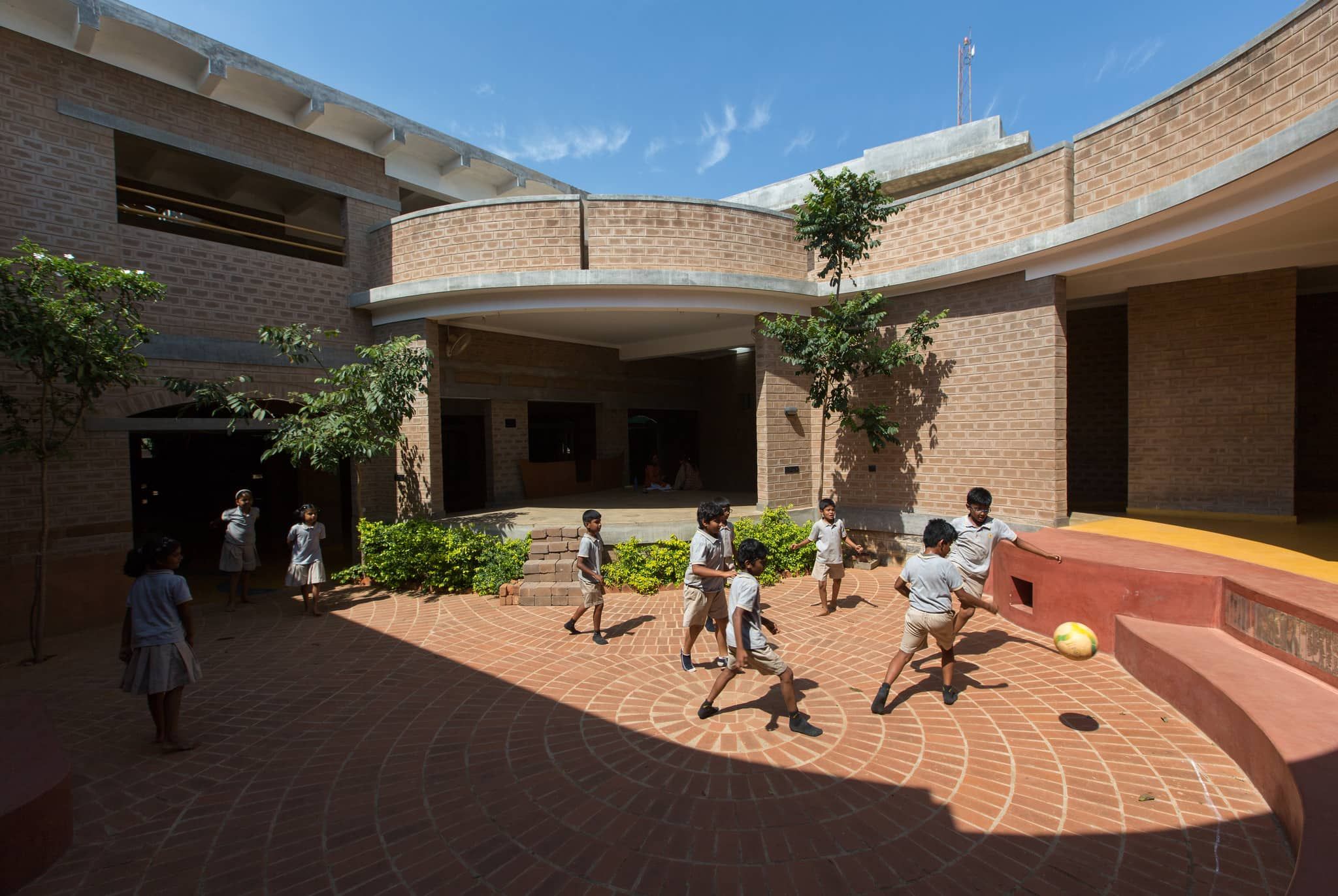 Children playing football in the central courtyard of the Yellow Train school by Biome