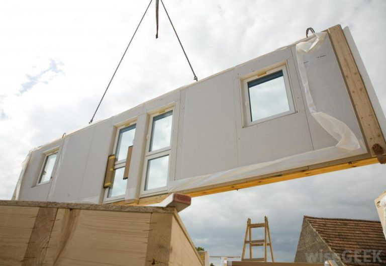 A Prefabricated wall with doors and windows attached is being placed on-site using a crane